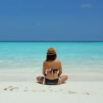 Woman sitting on a beach whilst on a wellness retreat